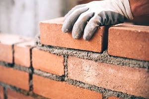 Close up of gloved hand laying bricks and mortar